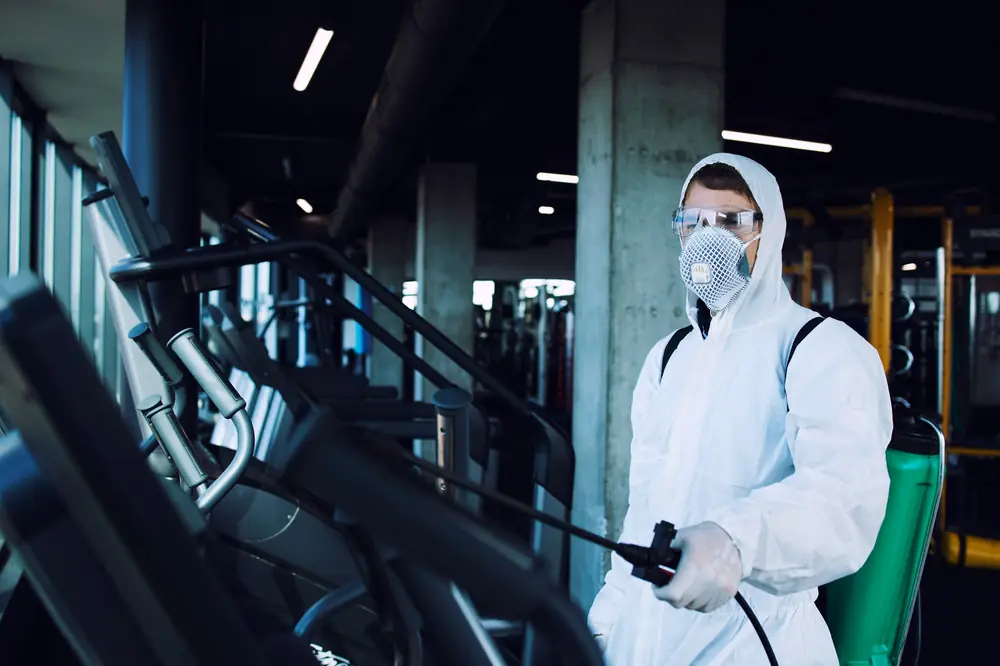 Pest control technician in protective suit and respirator spraying treatment